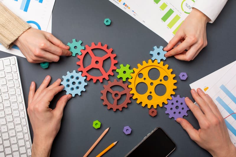 Équipe assemblant des engrenages colorés sur un bureau, symbolisant la collaboration et la méthode en marketing